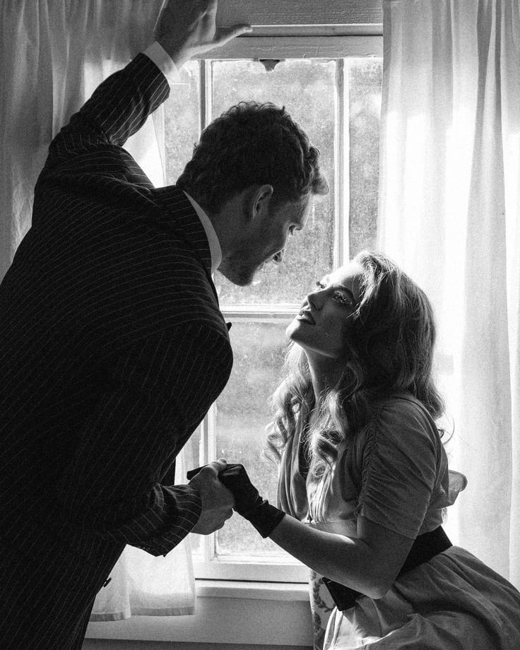 A man and a woman holding hands by a window, caught in intimate light